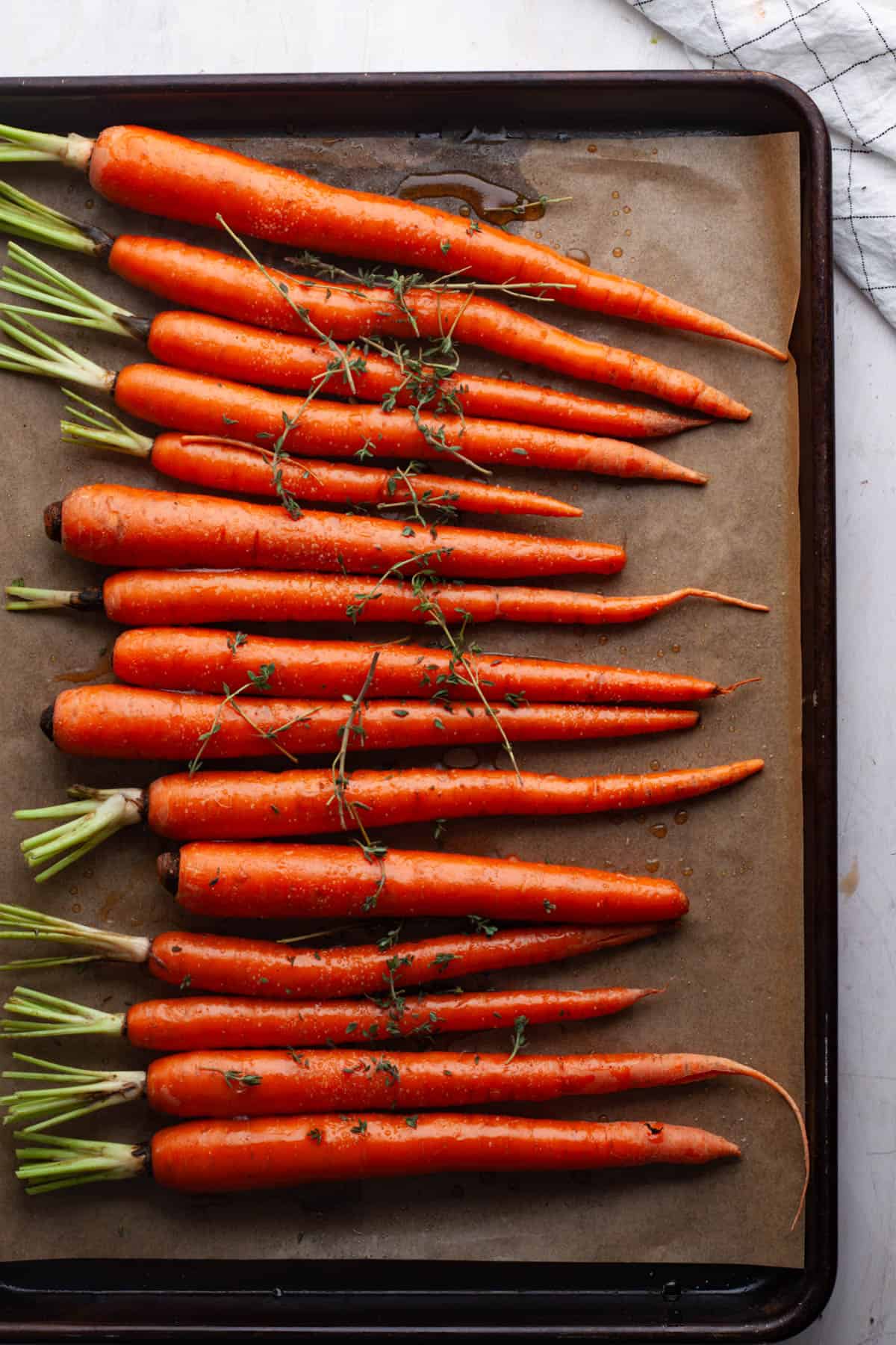 Thin whole carrots on a parchment-lined baking sheet topped with maple syrup and thyme.