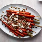Maple roasted carrots on a white platter topped with goat cheese and toasted pepitas.