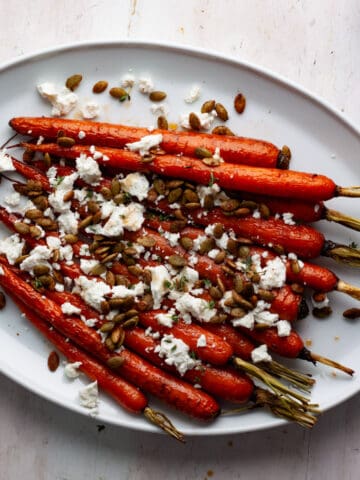 Maple roasted carrots on a white platter topped with goat cheese and toasted pepitas.
