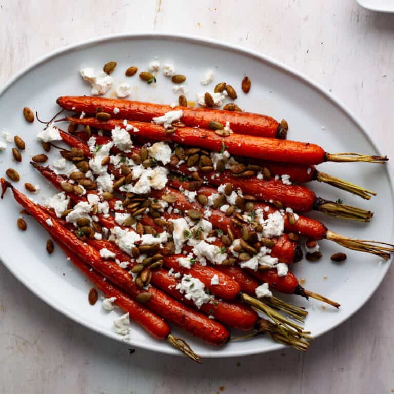 Maple roasted carrots on a white platter topped with goat cheese and toasted pepitas.