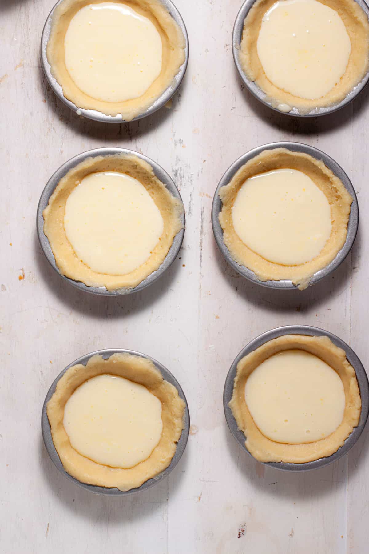 Mini peach custard pies getting assembled with the custard portion poured into the unbaked pie crust.