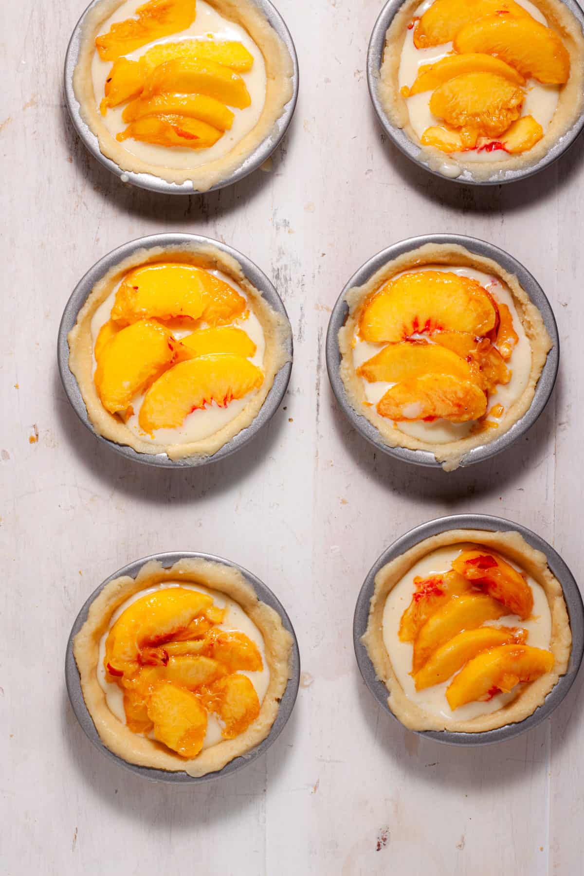 Mini peach custard pies getting assembled with sliced peaches added to the custard.