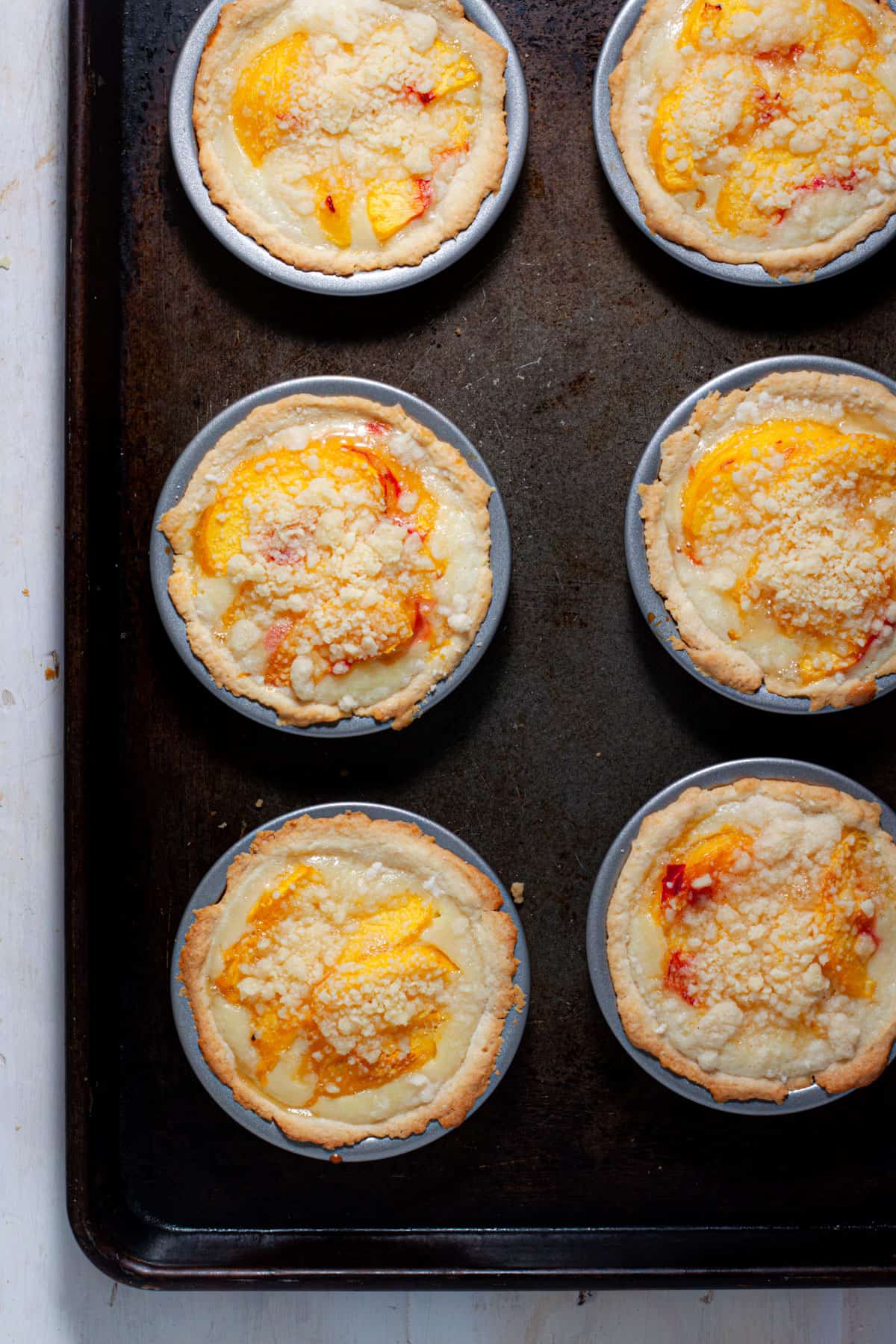Mini peach custard pies baked on a baking sheet to cool.