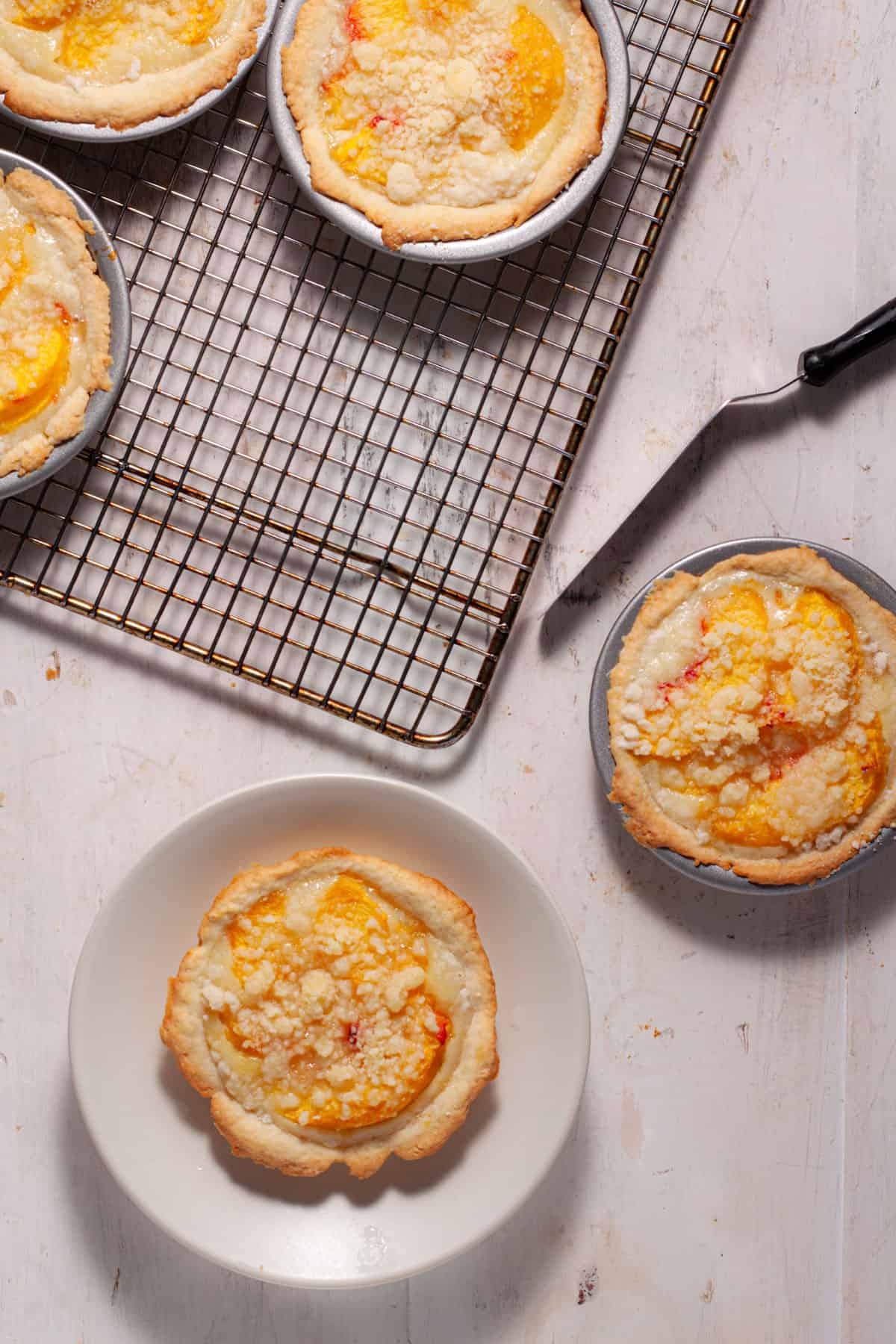Mini peach custard pies on a small plate and others cooling in the background.