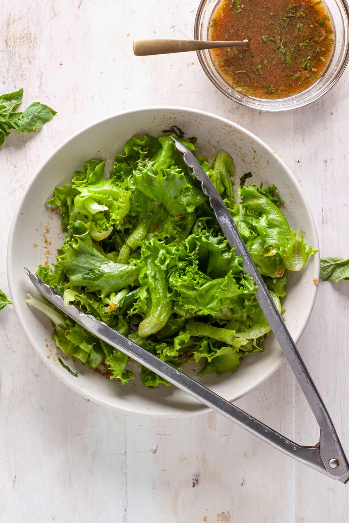 Salad greens in a bowl getting tossed with a basil balsamic vinaigrette.