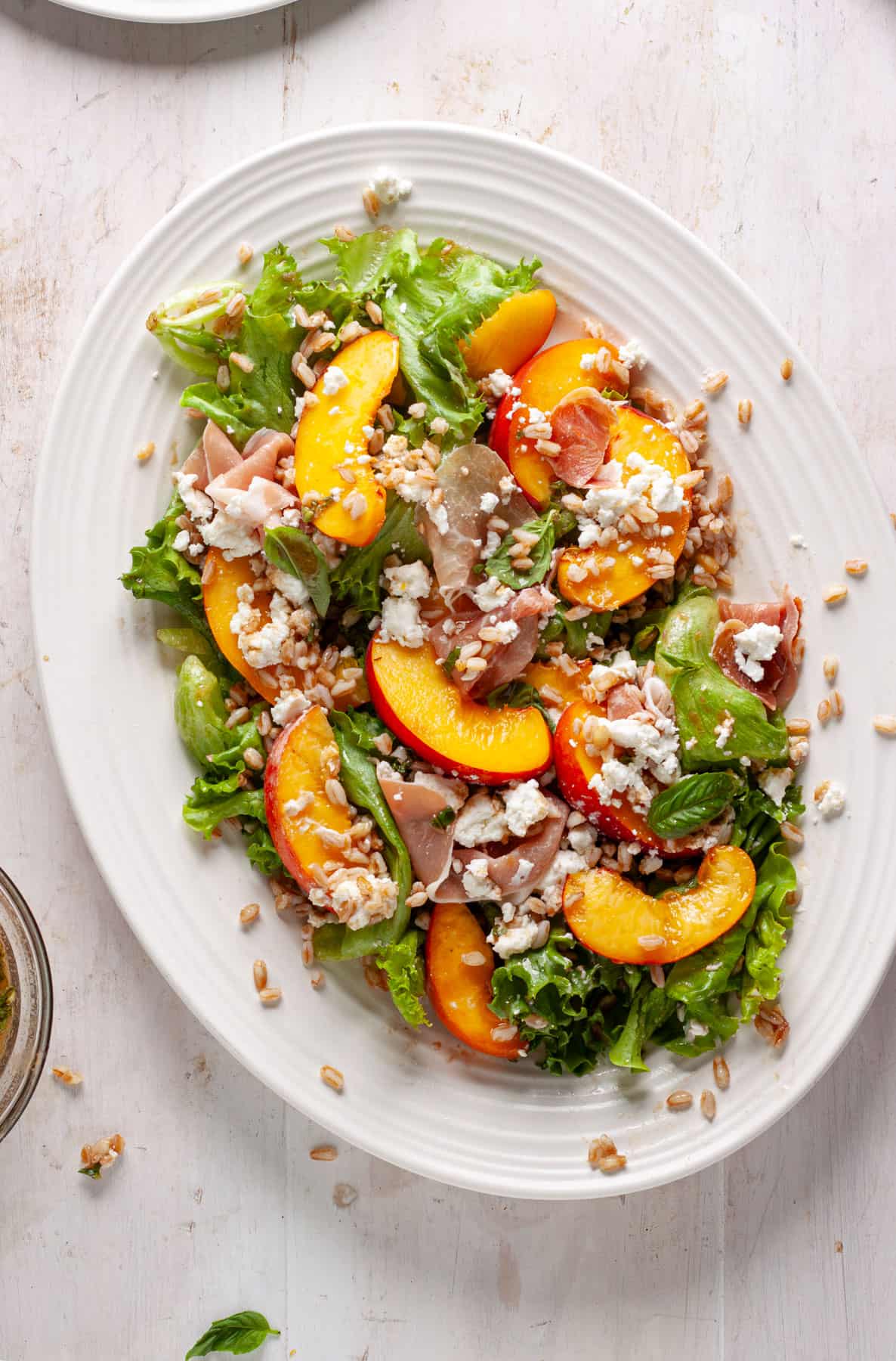 Peach and goat cheese salad on a white platter topped with prosciutto and farro.