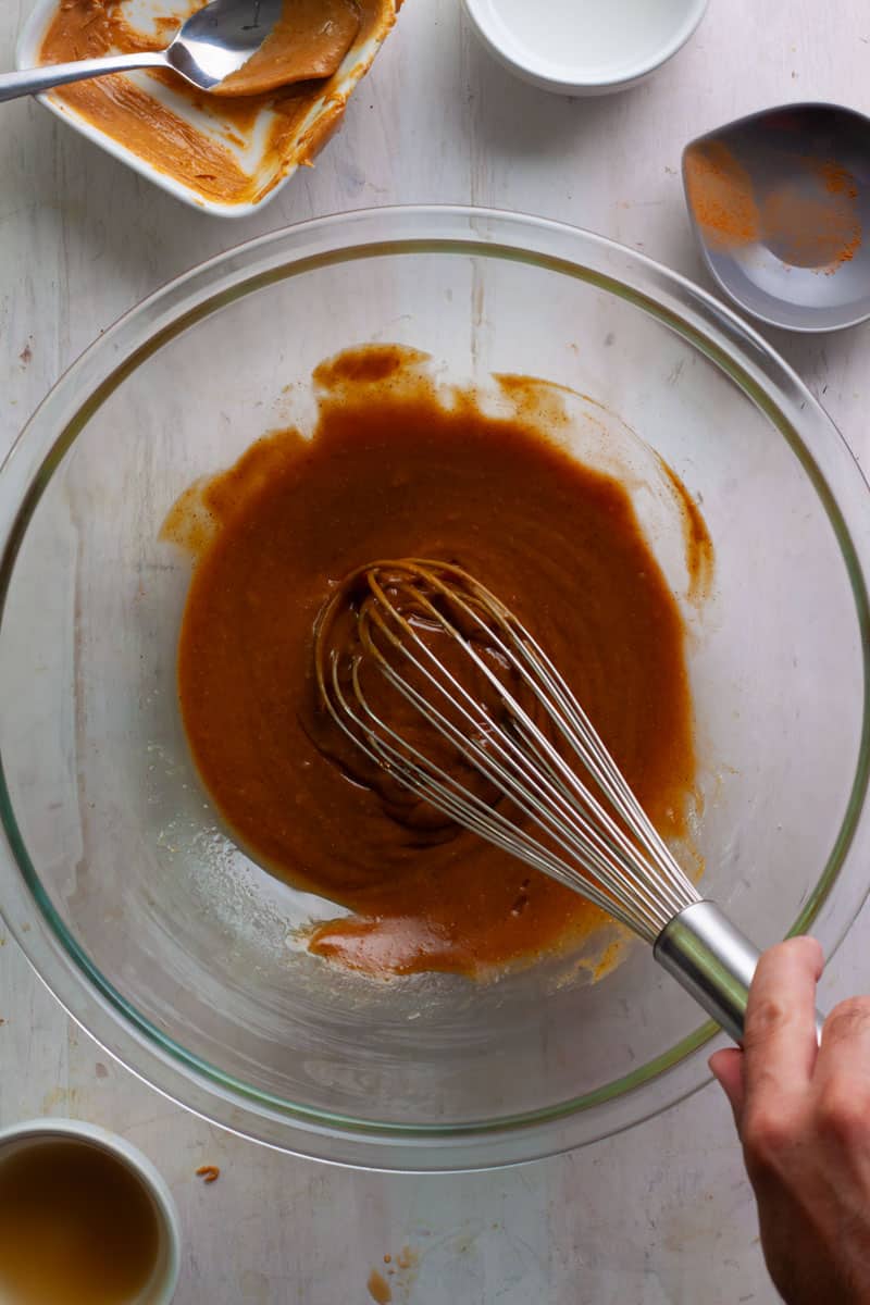 Wet ingredients for peanut butter granola in a large bowl with a whisk stirring it together.