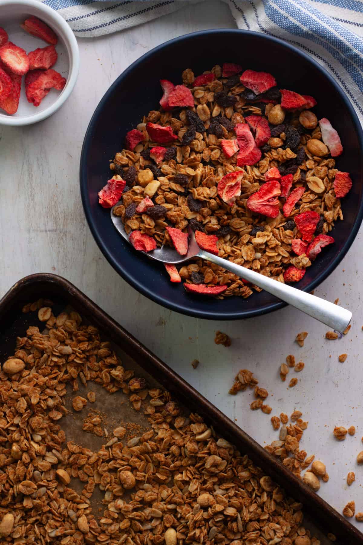 Peanut butter granola on a baking sheet and a bowl topped with dried strawberries.
