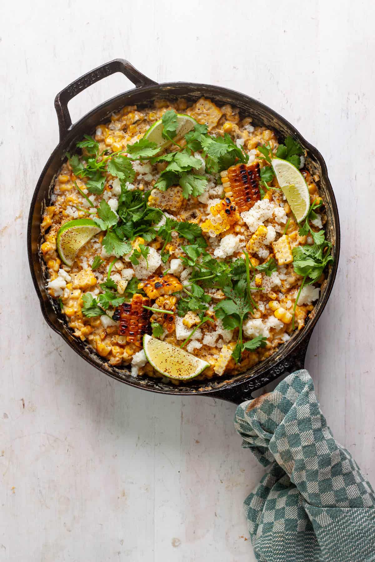 A skillet street corn dip topped with cilantro, lime wedges and cotija cheese.