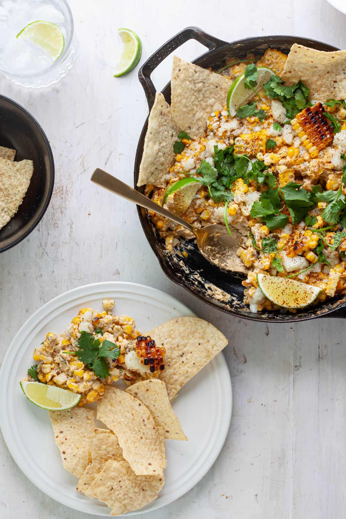 A small plate of chips with street corn dip and a skillet to the side with the dip.