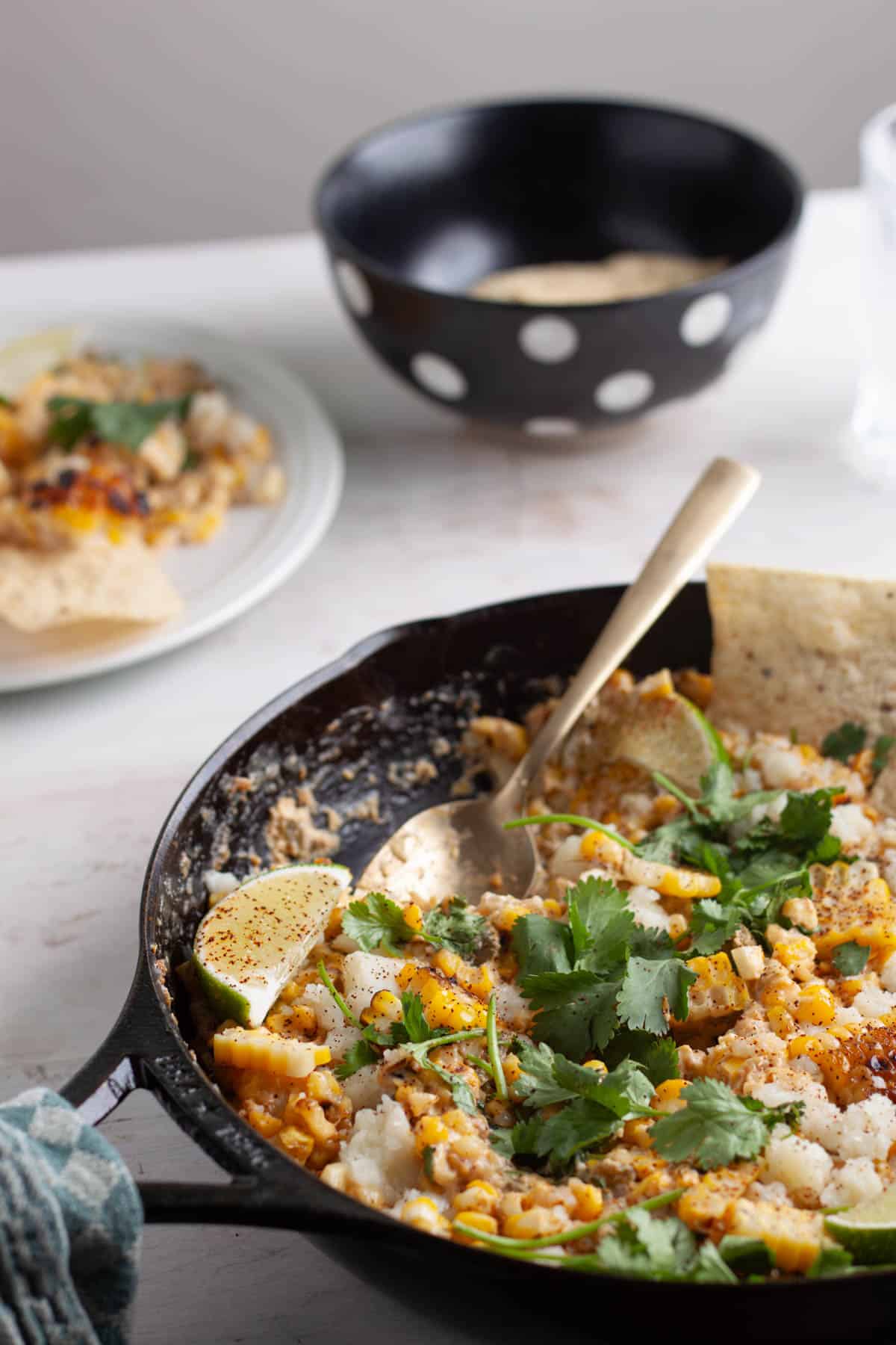 A skillet of Mexican street corn dip on a white table.