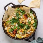 Skillet street corn dip topped with cilantro, cotija and lime wedges.