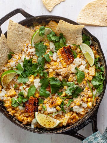 Skillet street corn dip topped with cilantro, cotija and lime wedges.