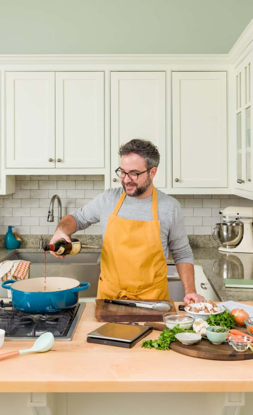 A chef pouring wine into a pot in a nice kitchen.