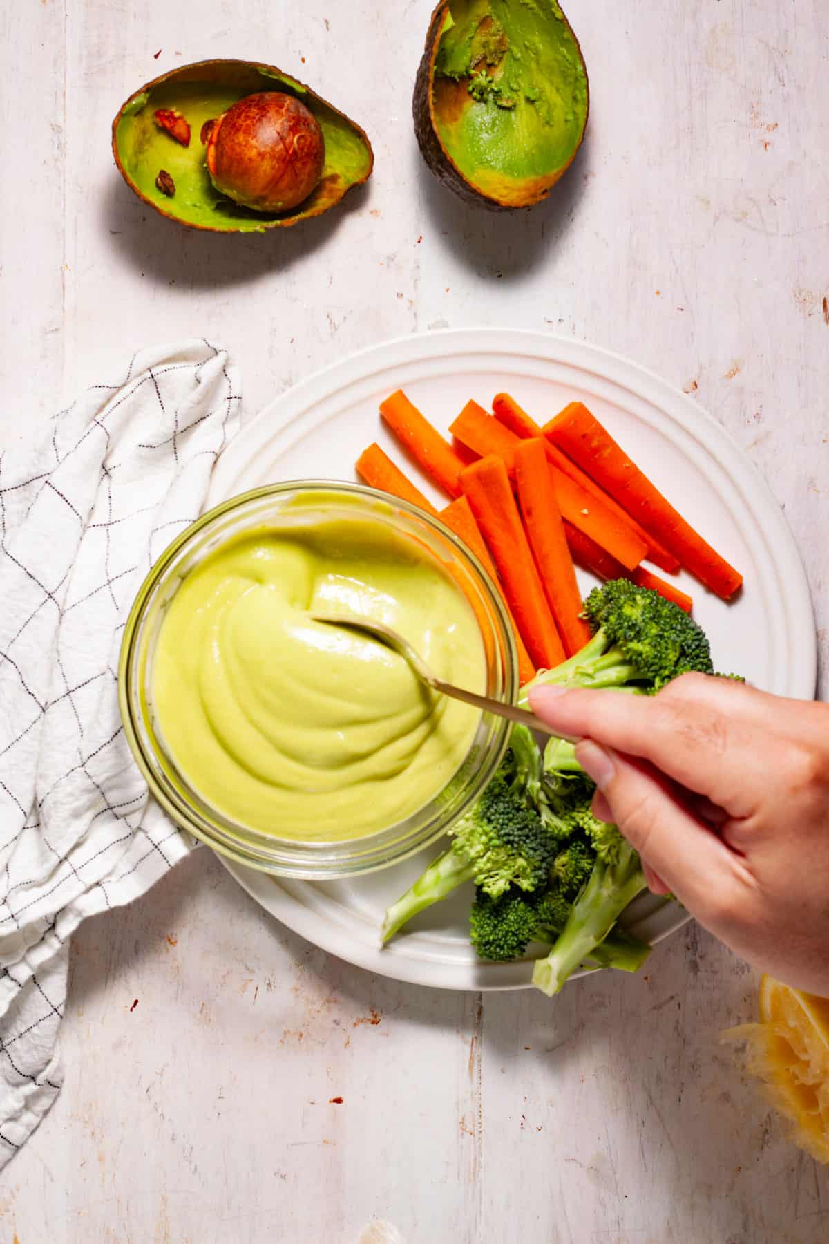 Avocado aioli getting stirred in a small bowl on a white plate with fresh veggies on the side.