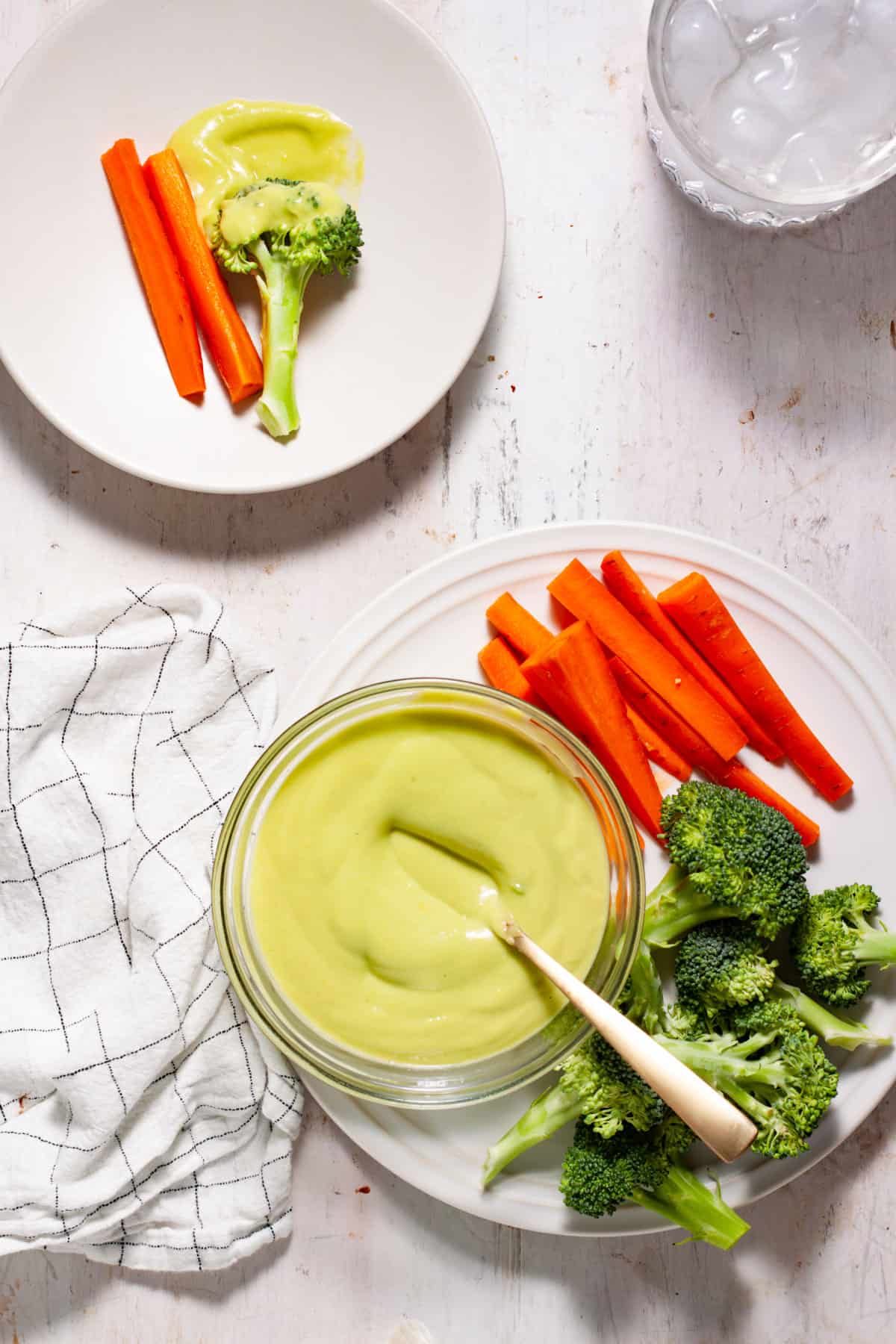 Avocado aioli getting stirred in a small bowl on a white plate with fresh veggies on the side.