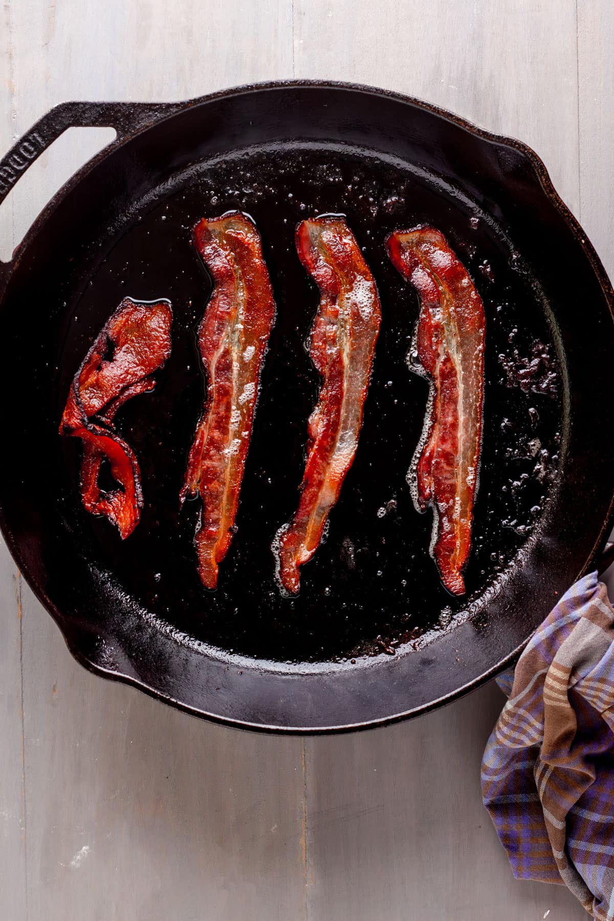 Bacon cooking in a large cast iron skillet.