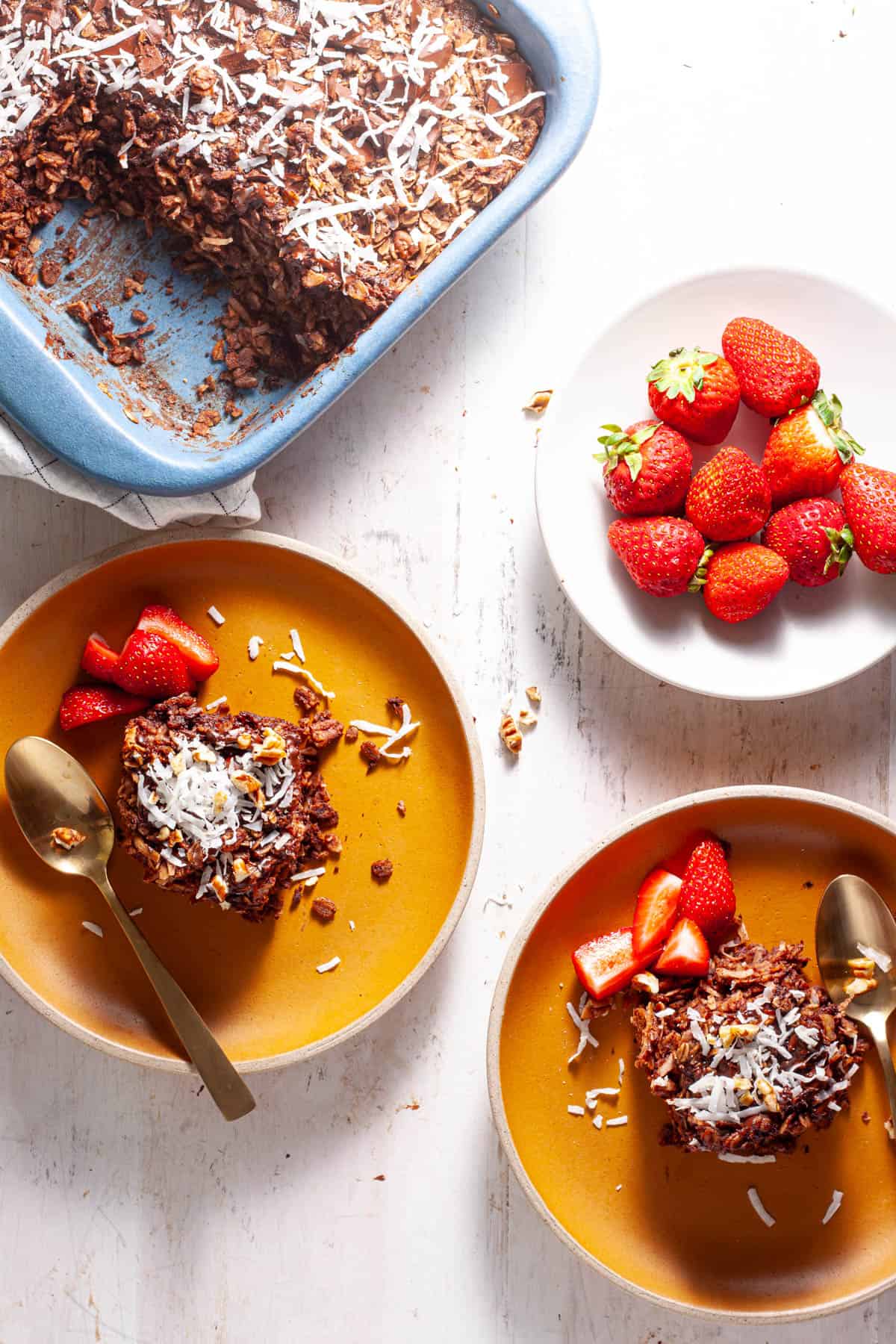 German chocolate baked oatmeal on a couple small plates with strawberries on the side.