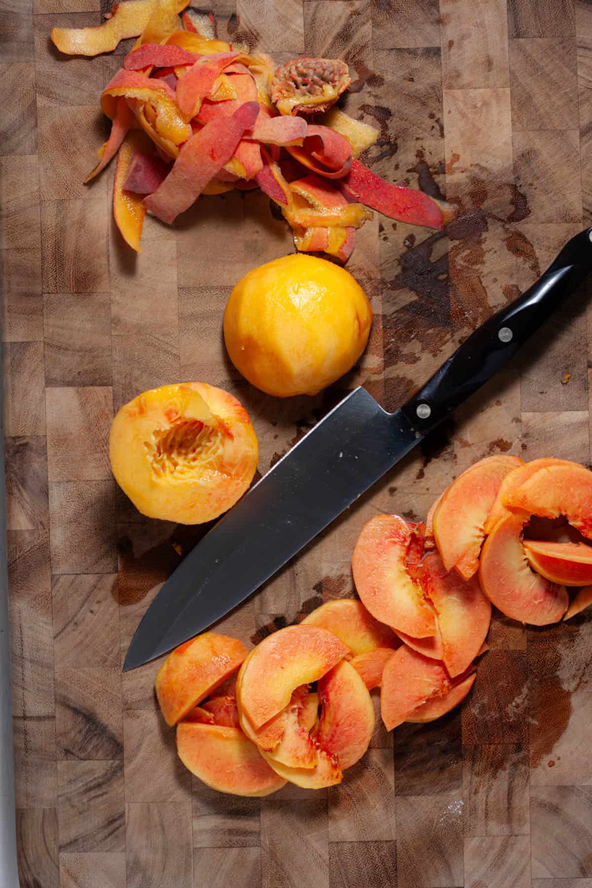 Peaches getting sliced on a wooden cutting board.