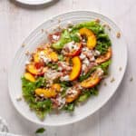 A platter of peach and goat cheese salad topped with farro and prosciutto.