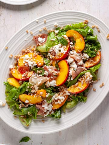 A platter of peach and goat cheese salad topped with farro and prosciutto.
