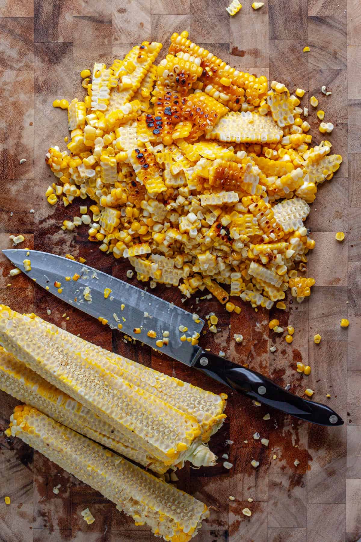 Charred corn getting cut off the cob on a cutting board.