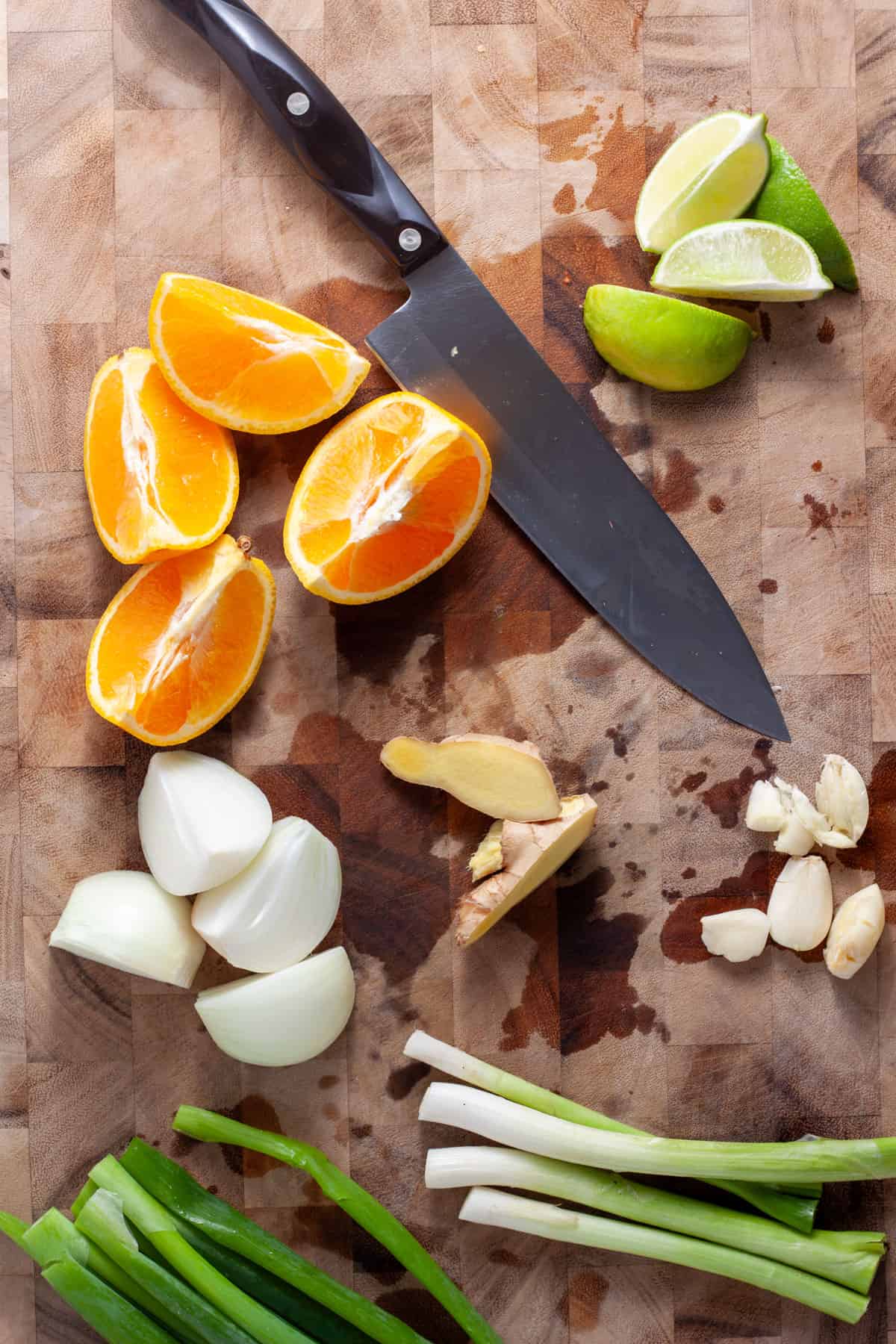 Scallions, ginger, garlic, orange, lime and onion chopped up on a cutting board.