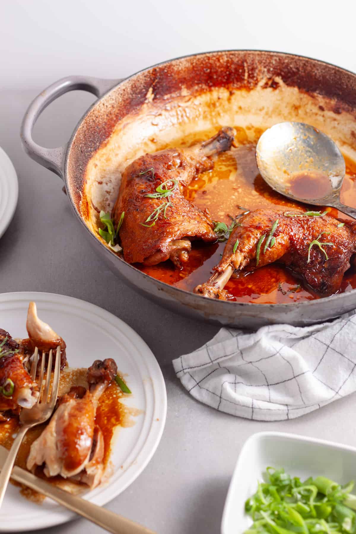 A pot of spicy chicken in a ginger, citrus and soy sauce on a gray table.