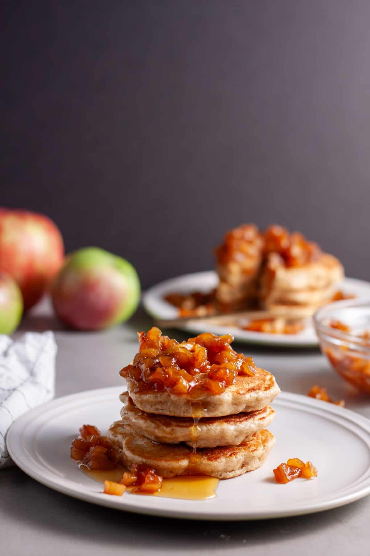 A stack of brown butter apple pancakes on a small plate topped with caramelized apples.