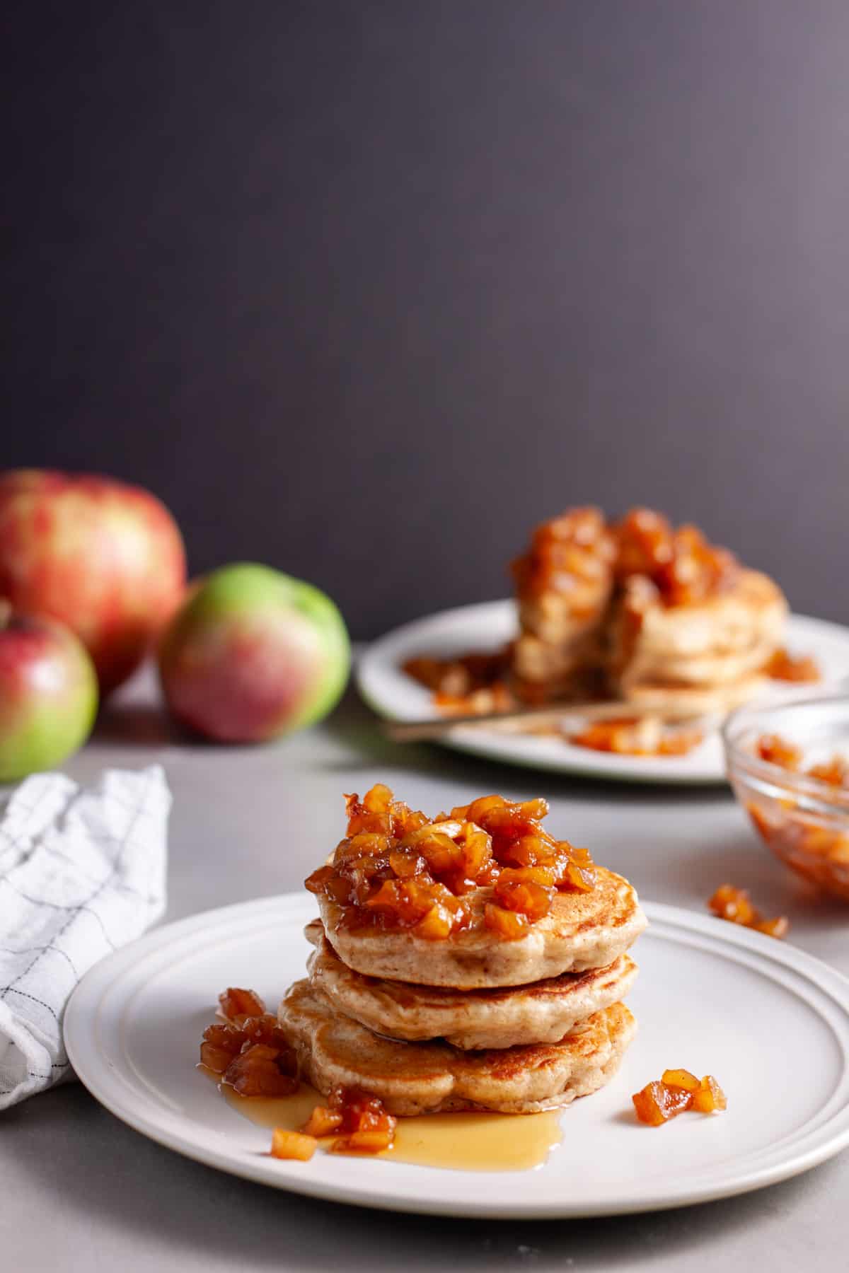 A stack of brown butter apple pancakes on a small plate topped with caramelized apples.