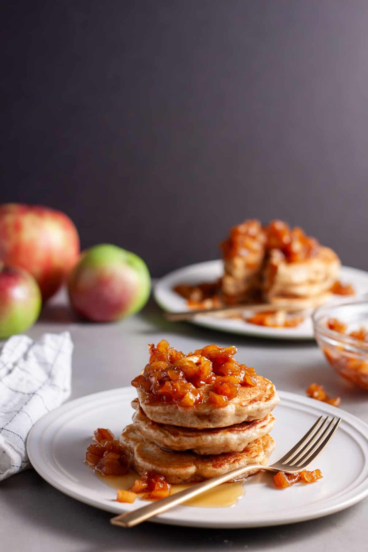A stack of brown butter apple pancakes on a small plate topped with caramelized apples.