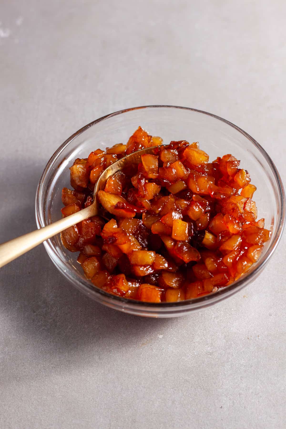 Caramelized apples in a small bowl with a gold spoon.