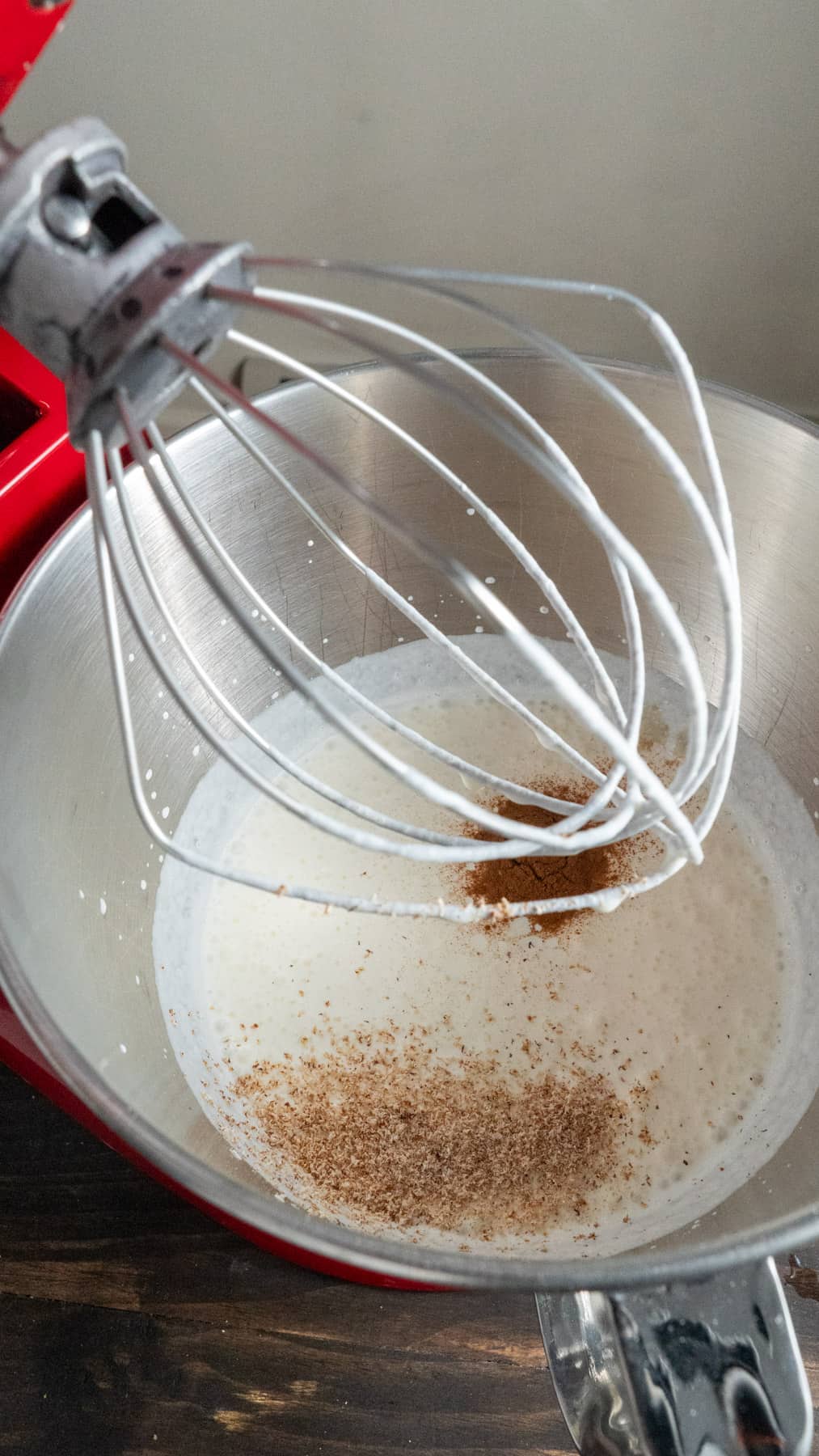 Heavy cream in a stand mixer with vanilla, cinnamon and nutmeg.