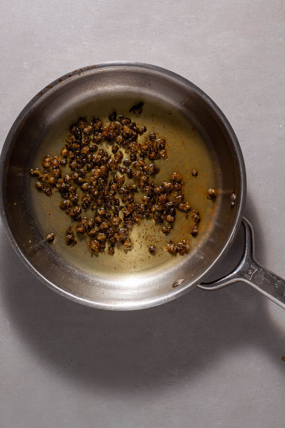 Capers frying in olive oil in a small skillet.