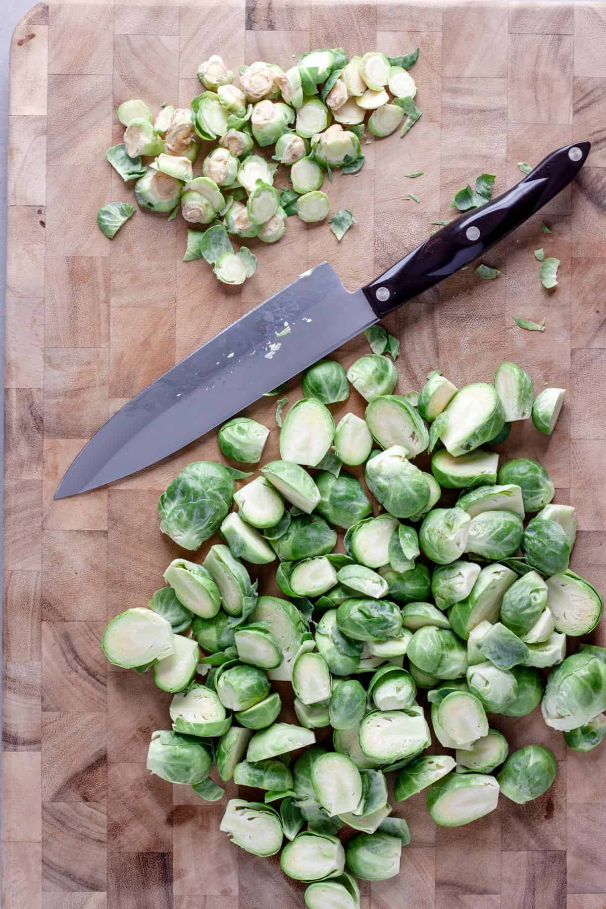 Brussels sprouts getting cut in half on a cutting board.