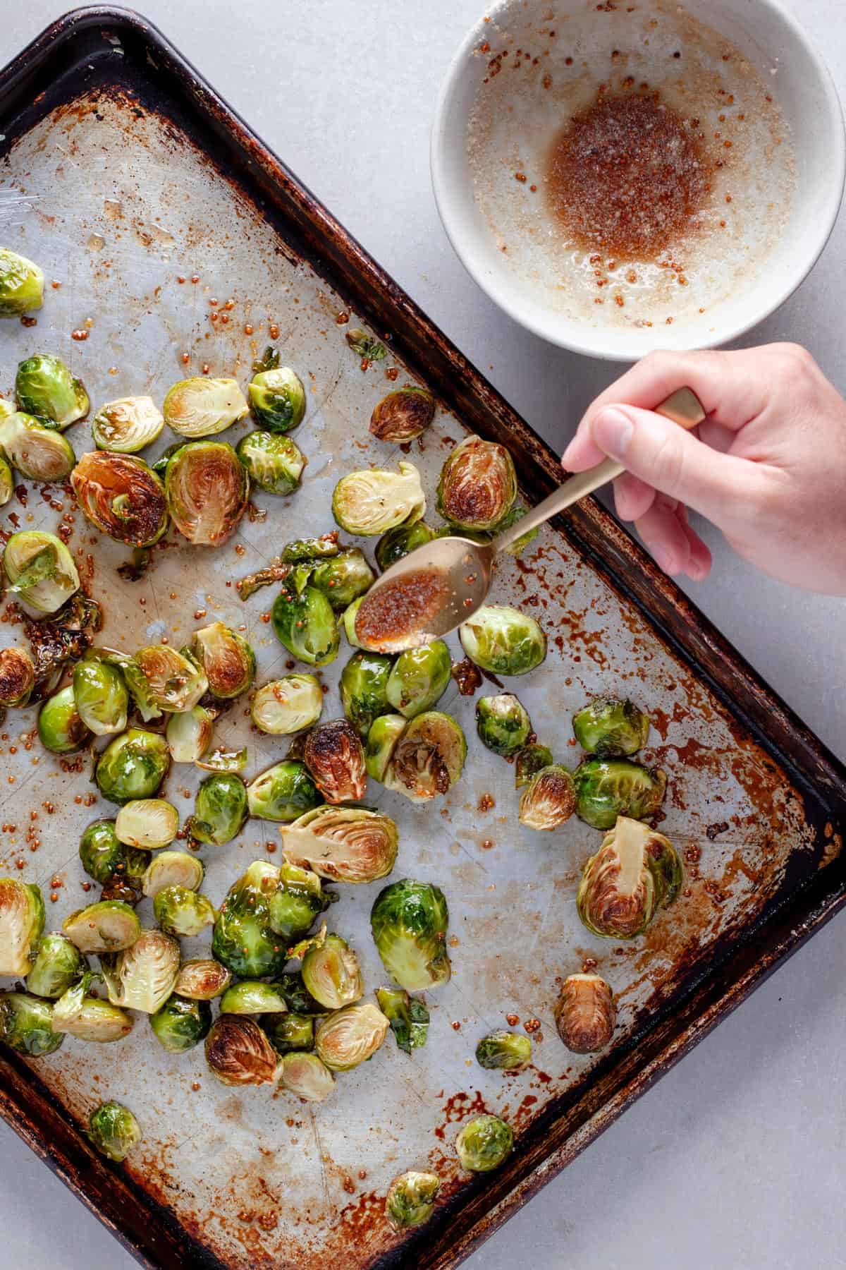 Roasted brussels sprouts get drizzled with maple balsamic vinegar sauce on a baking sheet.
