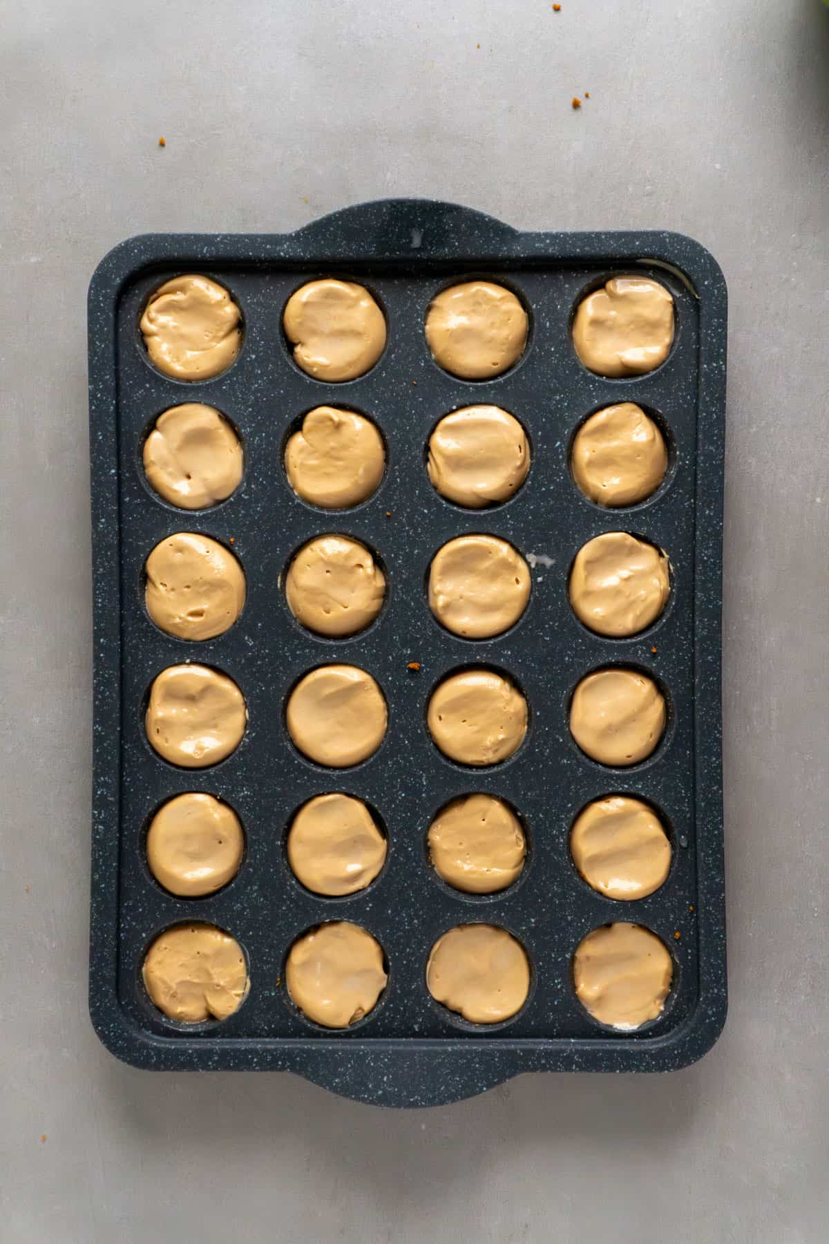 Mini biscoff cheesecakes in a mini muffin pan getting ready to freeze.