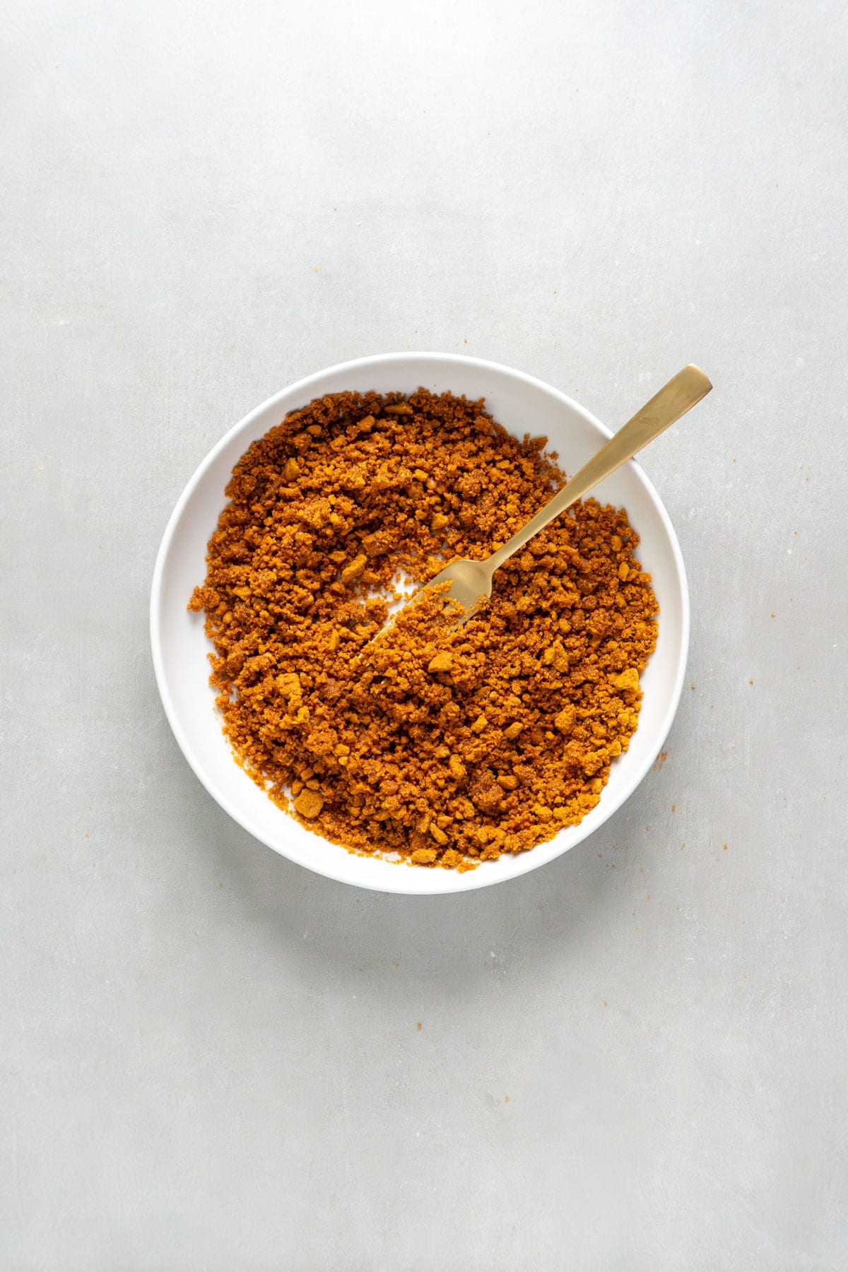 Ground Biscoff cookies in a small bowl mixed with melted butter.