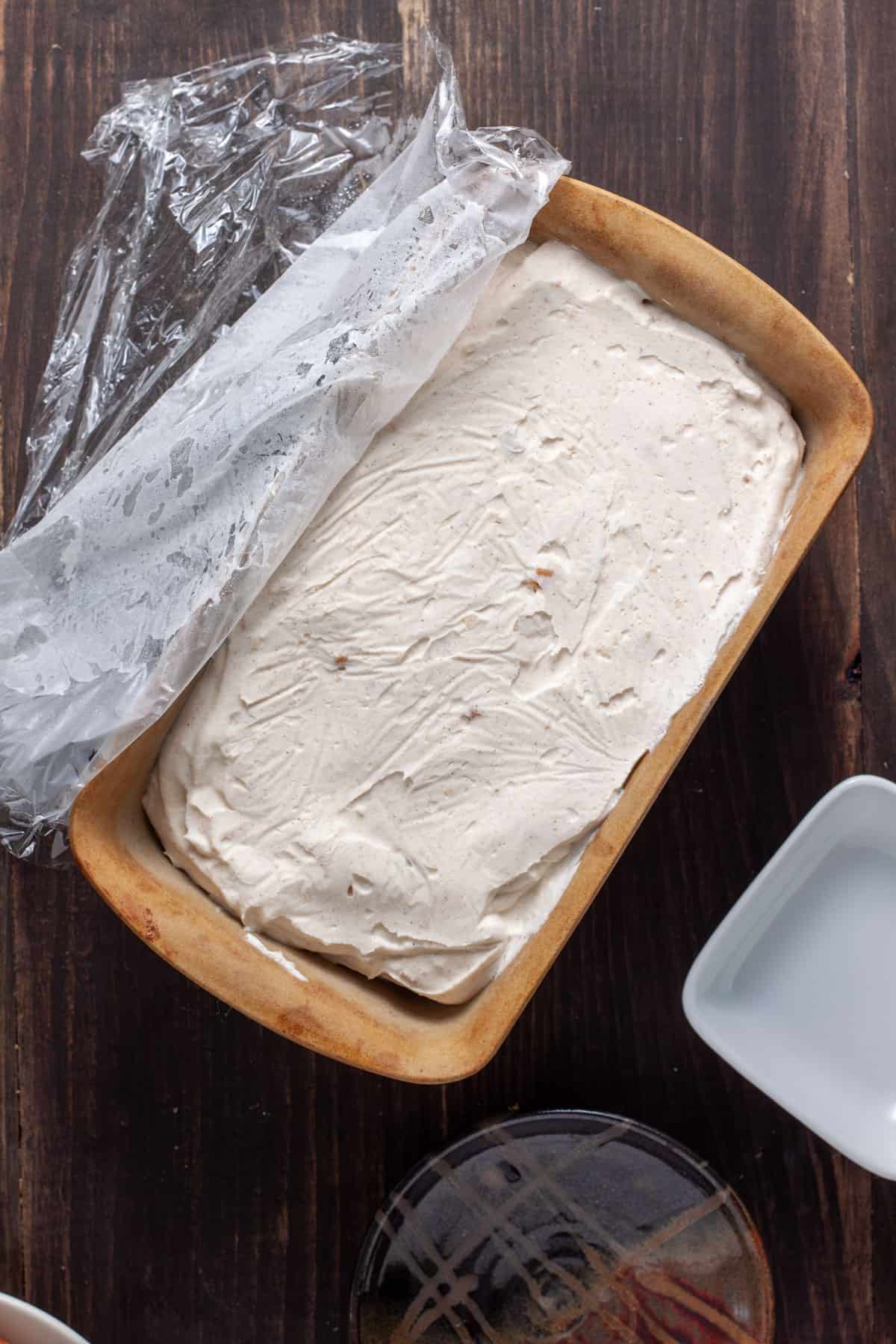 Cider donut ice cream in a loaf pan with the plastic wrap pulled off.