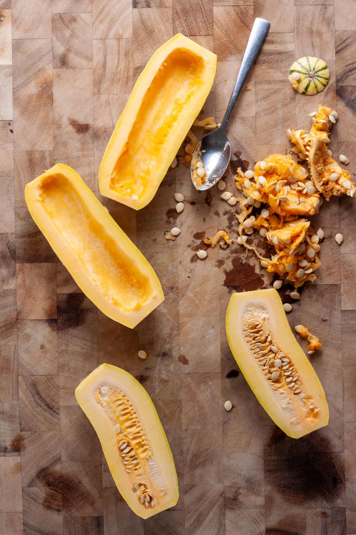Delicata squash on a cutting board with the inners scooped out with a spoon.