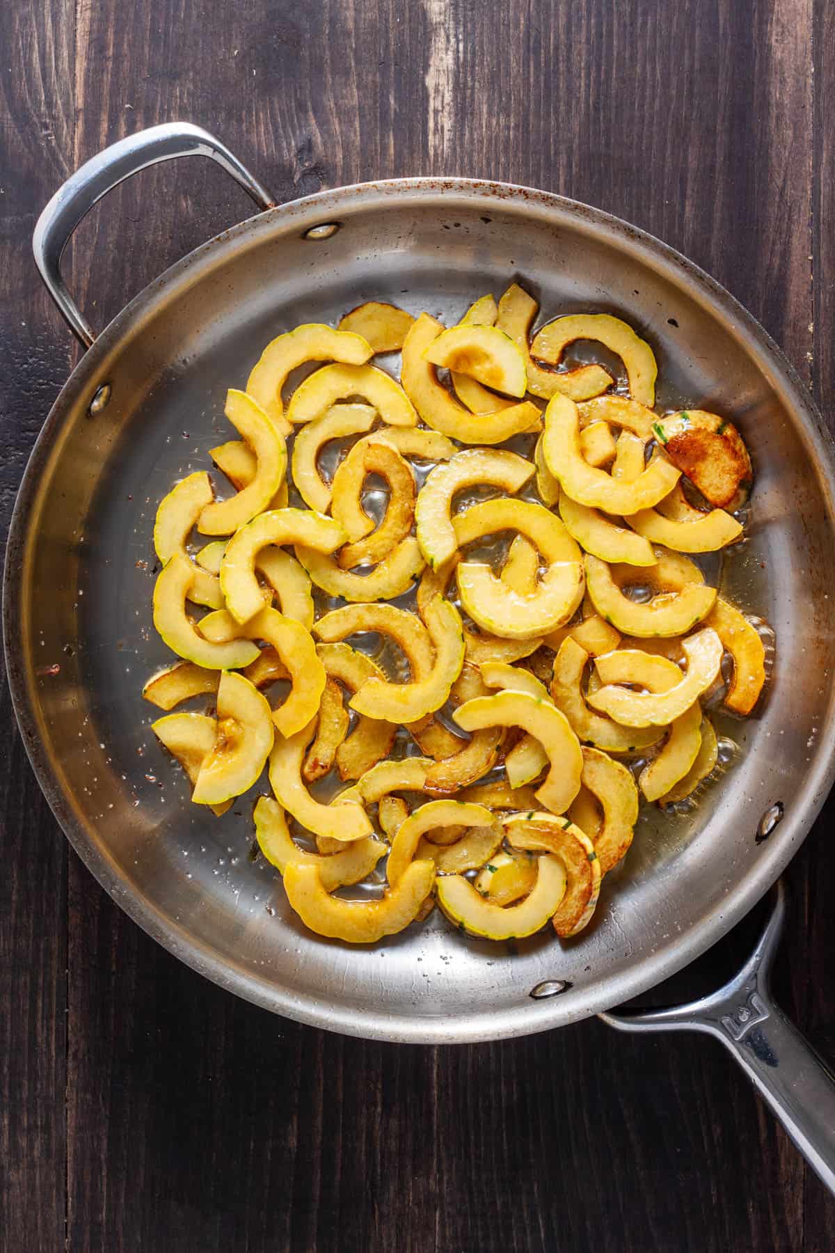Thinly sliced delicata squash cooking in a large skillet.