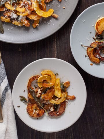 Sauteed delicata squash with crispy sage on a couple small plates and a larger platter to the side.