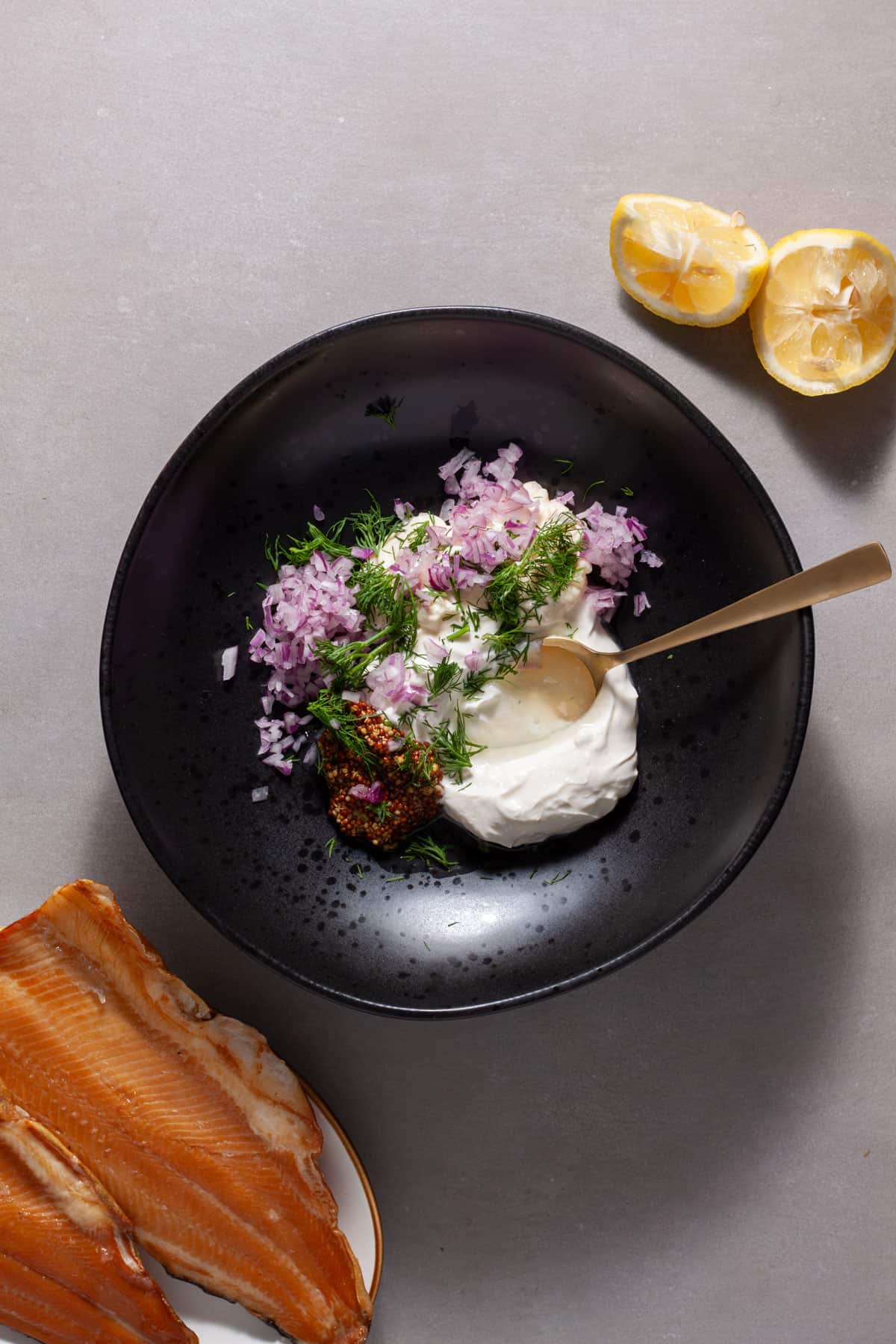 Smoked trout salad getting assembled in a black bowl with the sour cream, mayonnaise, mustard and shallot getting stirred.