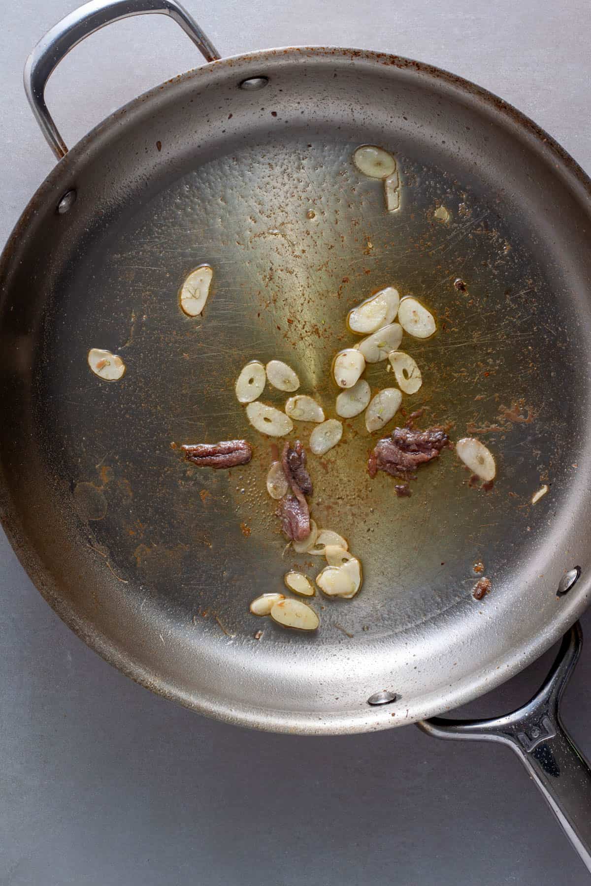 Anchovies and sliced garlic cooking in a large skillet with oil.