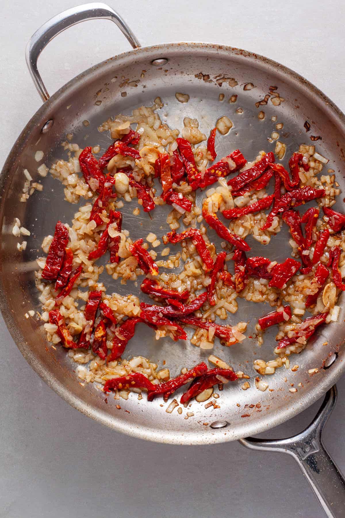 A large skillet with anchovies, garlic, sundried tomatoes and onions. 
