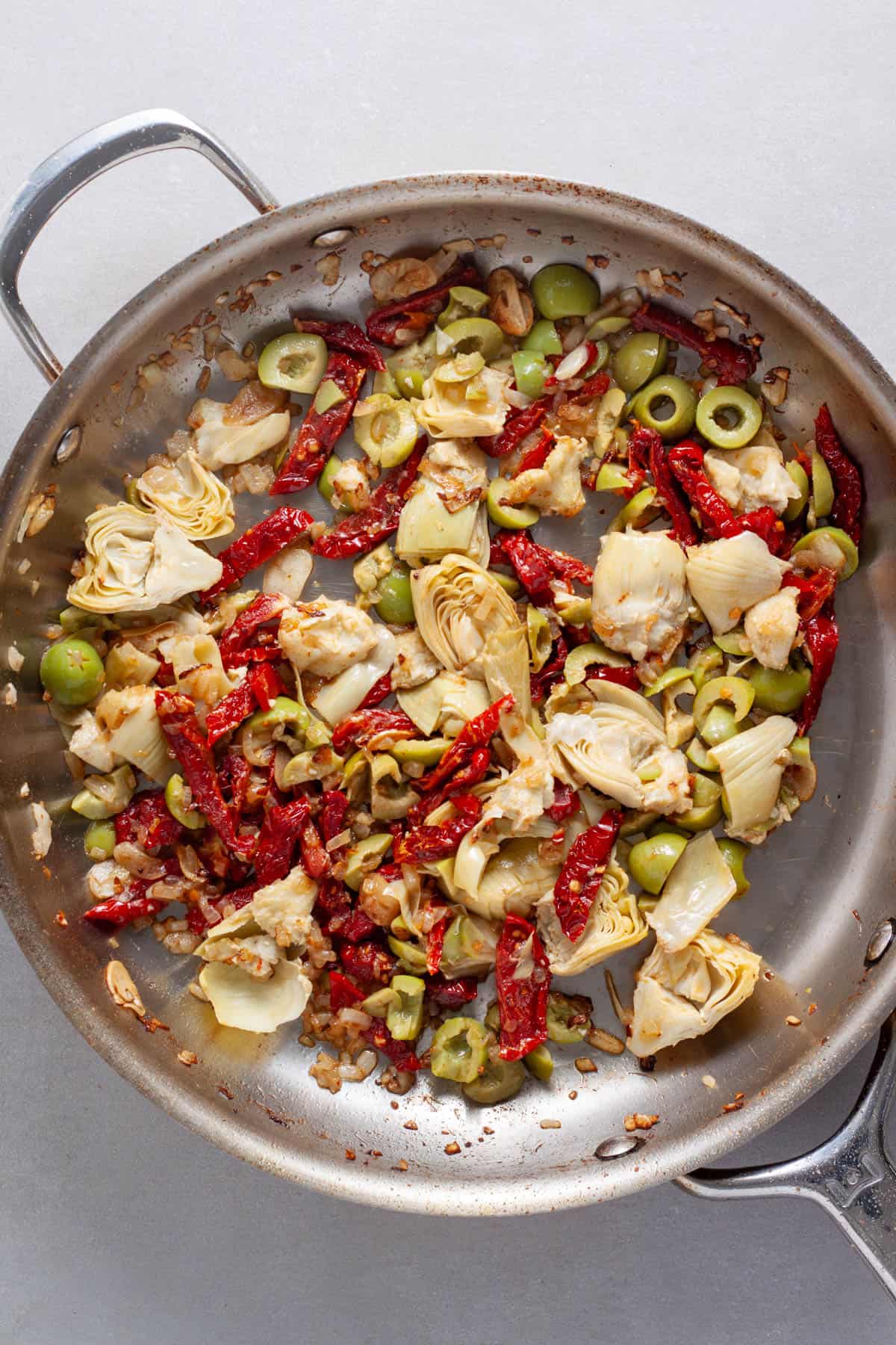 A large skillet with sun-dried tomatoes, artichokes, olives and onions.
