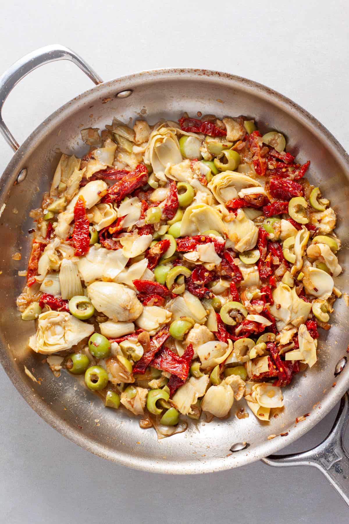 Sun-dried tomato and artichoke sauce for pasta cooking in a large skillet.