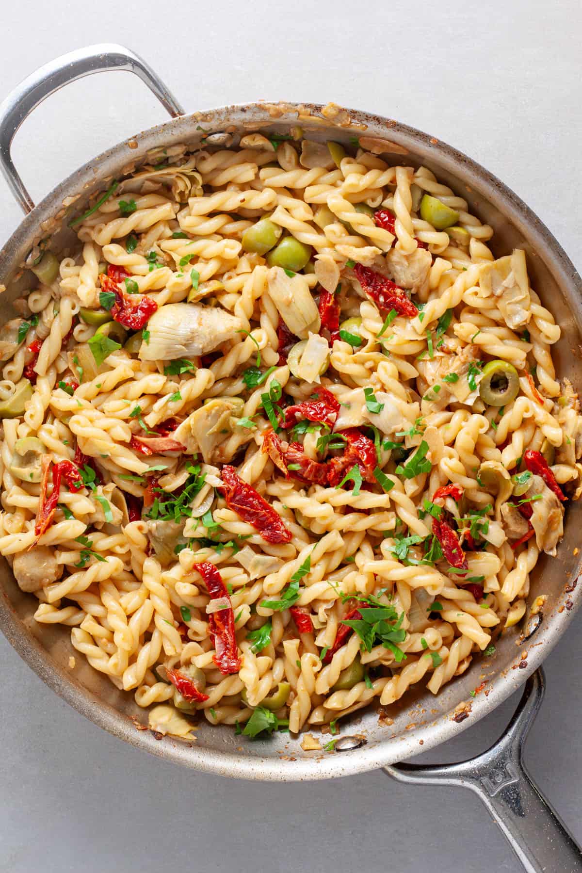 Sun-dried tomato and artichoke pasta cooking in a skillet topped with parsley.
