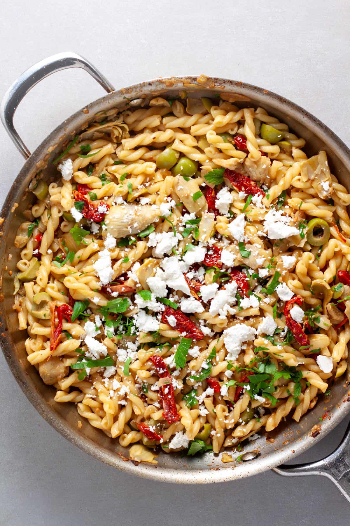 Sun-dried tomato and artichoke pasta in a skillet topped with ricotta salata cheese.