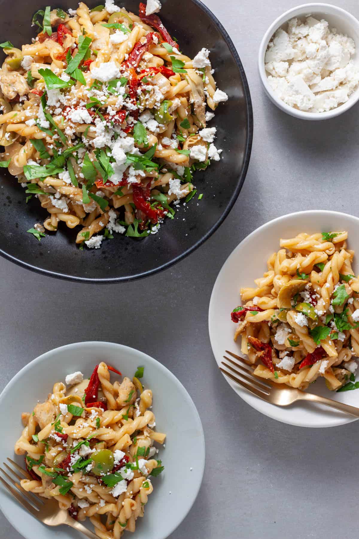 Sun-dried tomato and artichoke pasta in a large serving bowl with servings in a smaller plates.